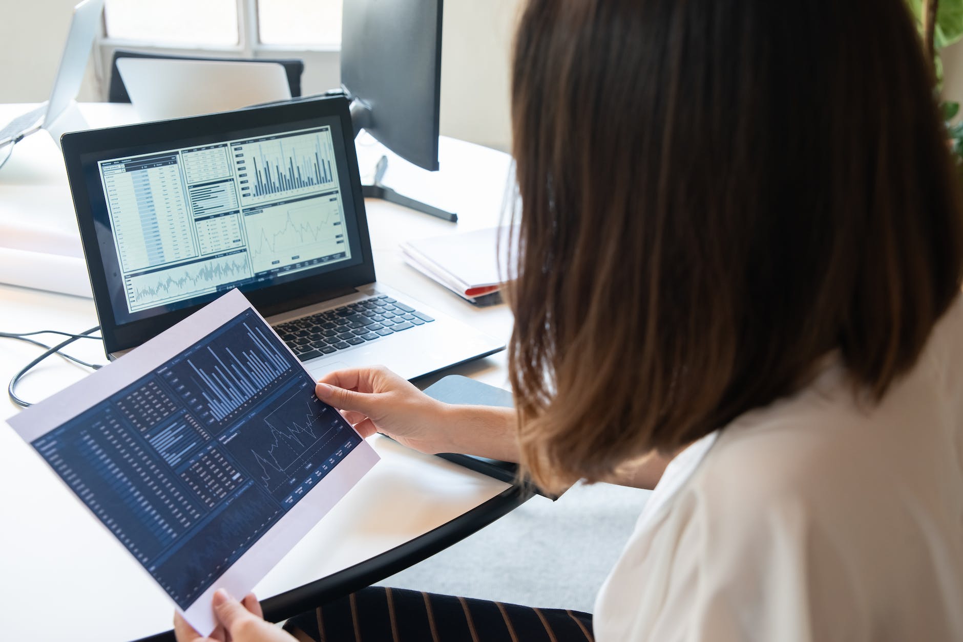 photo of a woman holding a paper with charts near her laptop